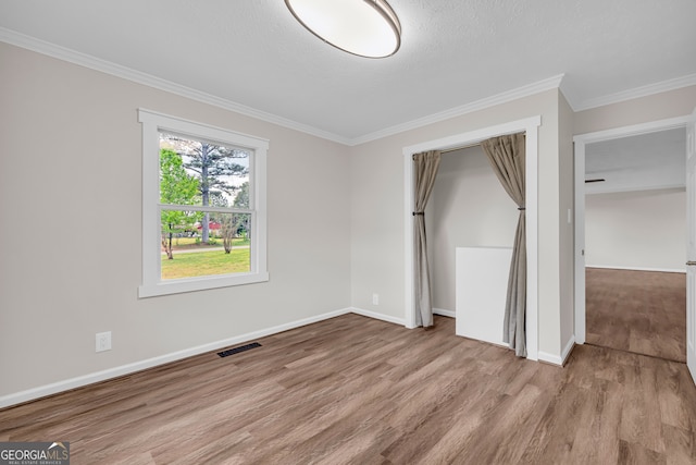 unfurnished bedroom featuring visible vents, baseboards, a closet, crown molding, and wood finished floors