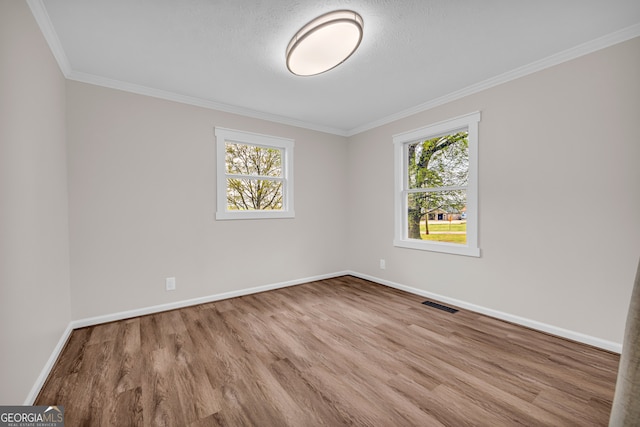 spare room featuring visible vents, baseboards, crown molding, and wood finished floors