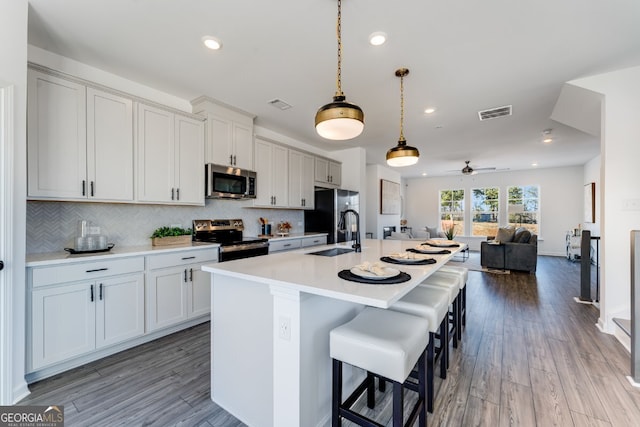 kitchen with light countertops, a sink, stainless steel appliances, open floor plan, and backsplash