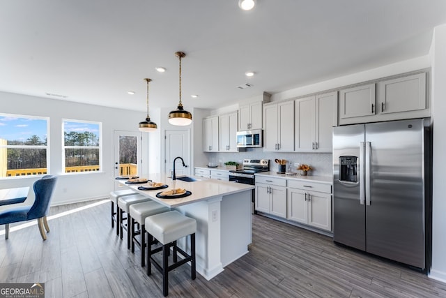 kitchen featuring appliances with stainless steel finishes, light countertops, a center island with sink, decorative backsplash, and a sink