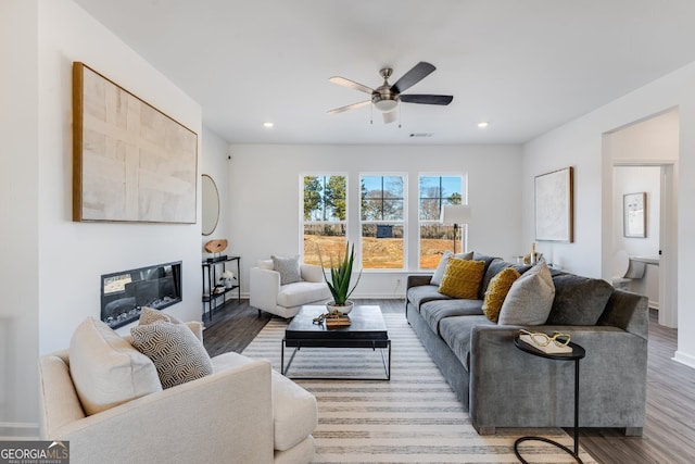 living area with ceiling fan, a glass covered fireplace, recessed lighting, wood finished floors, and baseboards