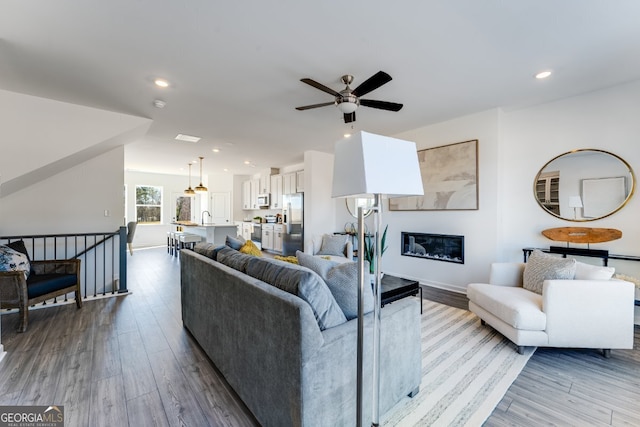 living area with wood finished floors, ceiling fan, a glass covered fireplace, and recessed lighting
