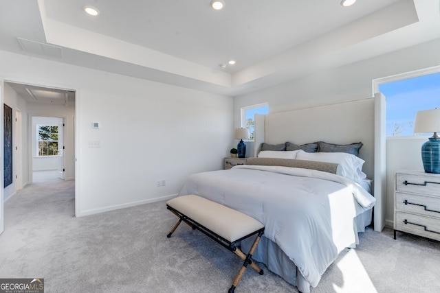 bedroom with a tray ceiling, multiple windows, attic access, and light colored carpet