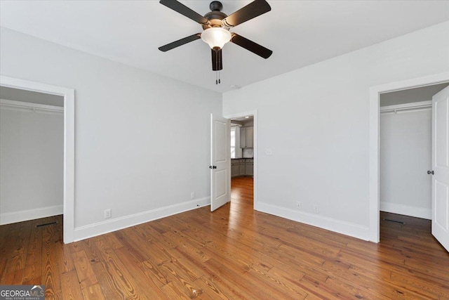 unfurnished bedroom featuring a closet, baseboards, a spacious closet, a ceiling fan, and hardwood / wood-style flooring