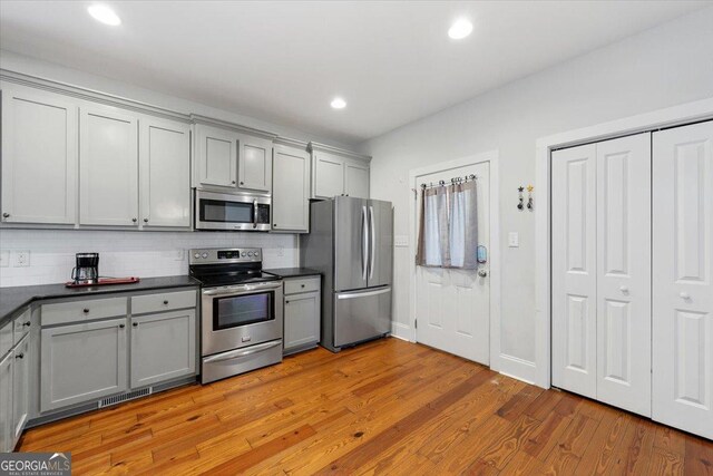 kitchen with light wood-type flooring, tasteful backsplash, gray cabinets, appliances with stainless steel finishes, and dark countertops