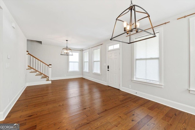 foyer featuring baseboards, an inviting chandelier, hardwood / wood-style flooring, and stairs