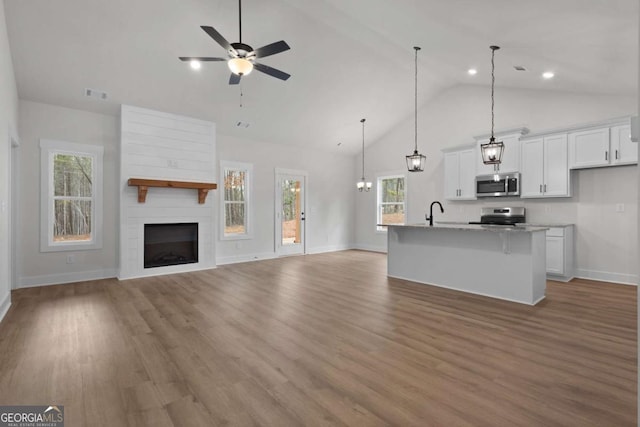 unfurnished living room with baseboards, a fireplace, visible vents, ceiling fan, and light wood finished floors