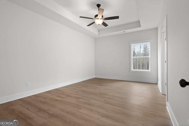 unfurnished room with a tray ceiling, baseboards, ceiling fan, and wood finished floors