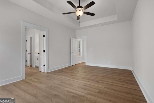 unfurnished bedroom featuring baseboards, a raised ceiling, wood finished floors, and a ceiling fan