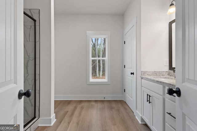full bathroom with a shower stall, vanity, baseboards, and wood finished floors
