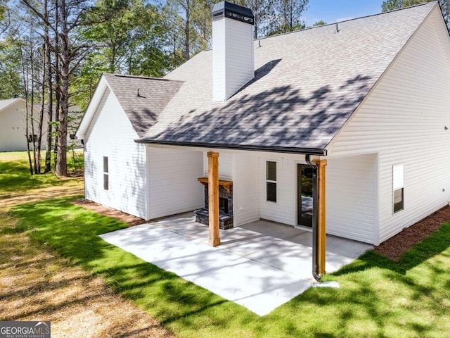 back of property with a patio, a chimney, a shingled roof, and a lawn