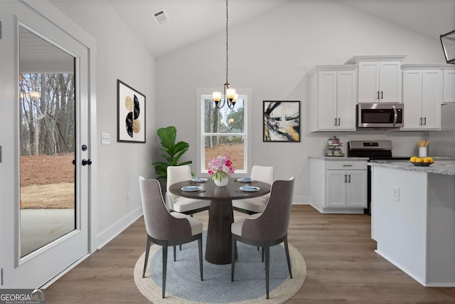 dining space with a chandelier, wood finished floors, visible vents, and lofted ceiling