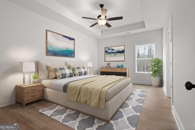 bedroom featuring a tray ceiling, baseboards, and light wood-type flooring