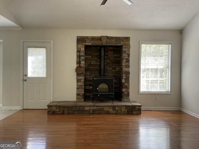 living area featuring a wood stove, ceiling fan, wood finished floors, and a healthy amount of sunlight