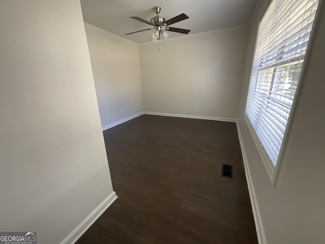 unfurnished room featuring crown molding, dark wood finished floors, a ceiling fan, baseboards, and visible vents
