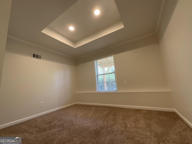 empty room featuring a raised ceiling, dark carpet, baseboards, visible vents, and ornamental molding