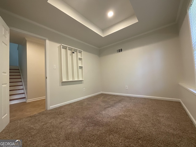 carpeted empty room featuring stairway, ornamental molding, a tray ceiling, and visible vents