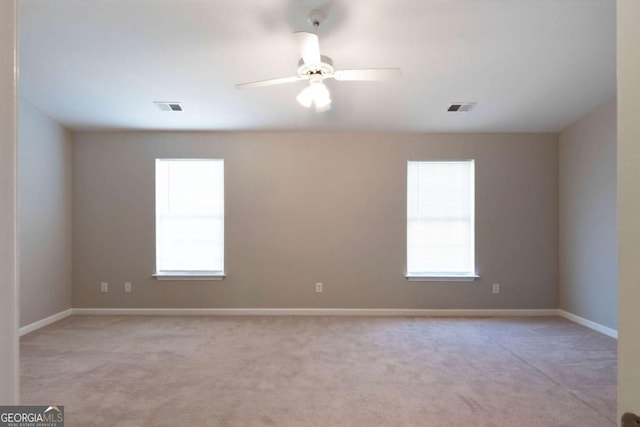 carpeted spare room with plenty of natural light, visible vents, and ceiling fan