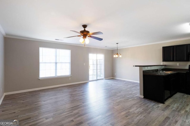 unfurnished living room with baseboards, a sink, crown molding, wood finished floors, and ceiling fan with notable chandelier