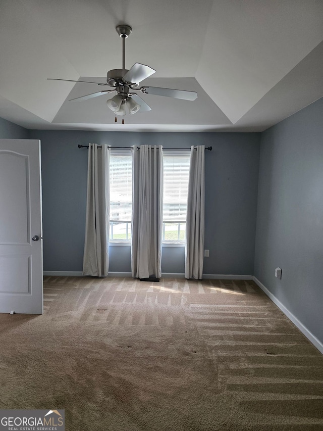 carpeted empty room featuring baseboards, a tray ceiling, and a ceiling fan