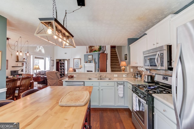 kitchen featuring a sink, a textured ceiling, appliances with stainless steel finishes, open floor plan, and dark wood finished floors