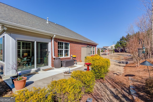 rear view of house featuring a shingled roof and brick siding