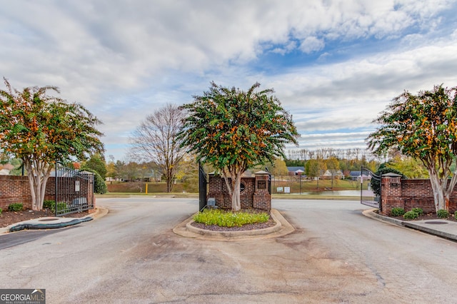 view of road featuring a gate, curbs, a gated entry, and a water view