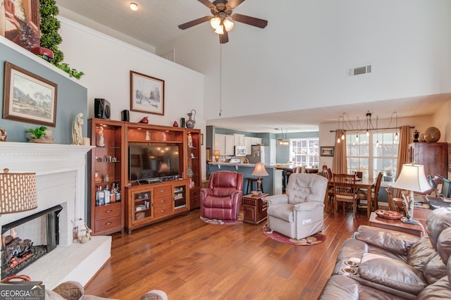 living room with a fireplace with raised hearth, ceiling fan, visible vents, a towering ceiling, and wood finished floors