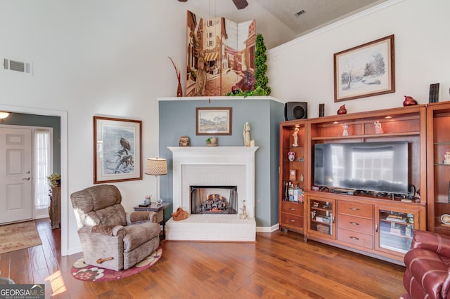 living room with a fireplace, wood finished floors, visible vents, and high vaulted ceiling