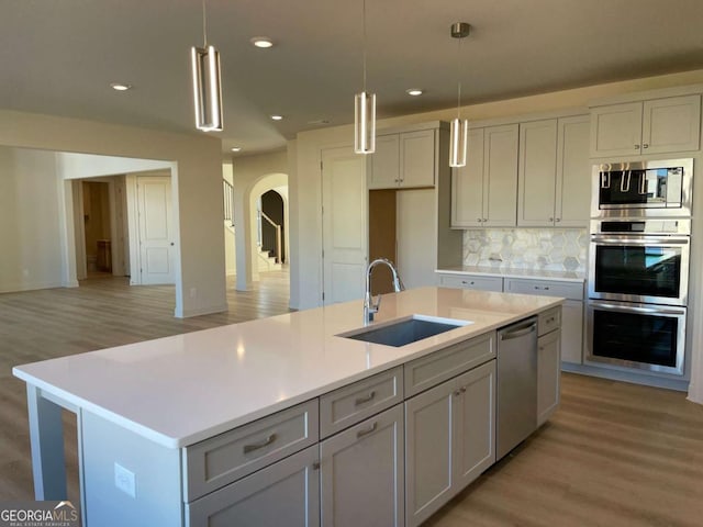 kitchen featuring an island with sink, arched walkways, a sink, stainless steel appliances, and backsplash