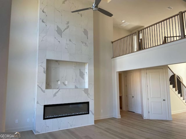 unfurnished living room with a towering ceiling, a ceiling fan, wood finished floors, stairs, and a high end fireplace