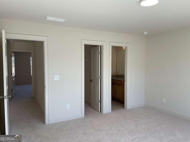 unfurnished bedroom featuring ensuite bathroom, baseboards, a walk in closet, and light colored carpet