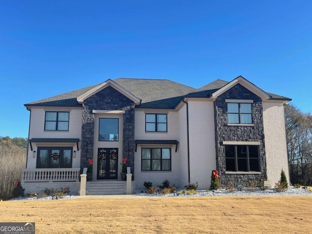 view of front of house featuring brick siding, french doors, stone siding, and roof with shingles