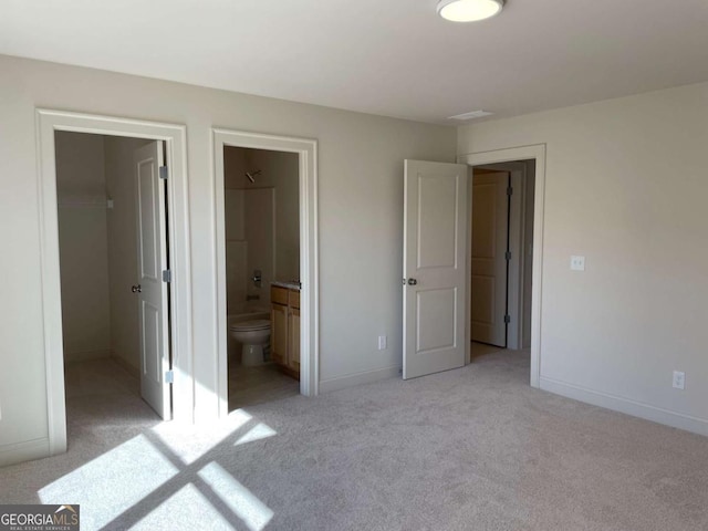 unfurnished bedroom featuring ensuite bathroom, a closet, light colored carpet, a walk in closet, and baseboards
