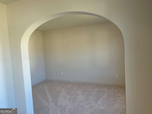 spare room featuring baseboards, arched walkways, and light carpet