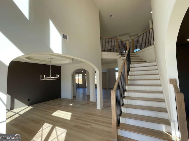 stairway with arched walkways, wood finished floors, a towering ceiling, and visible vents