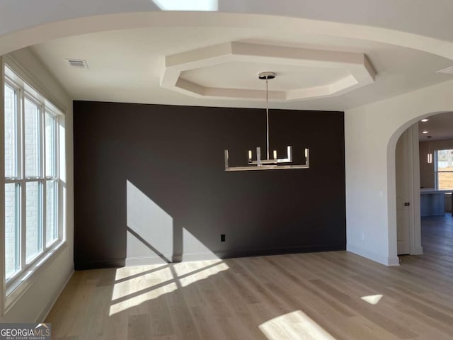 unfurnished dining area with visible vents, a raised ceiling, arched walkways, a healthy amount of sunlight, and wood finished floors