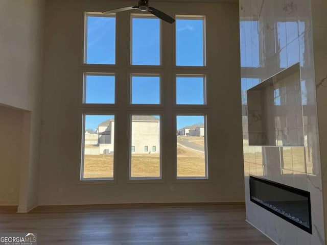 unfurnished living room featuring a ceiling fan, plenty of natural light, a high ceiling, and wood finished floors