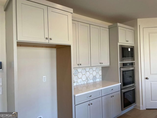 kitchen featuring gray cabinets, light countertops, appliances with stainless steel finishes, backsplash, and light wood-style flooring