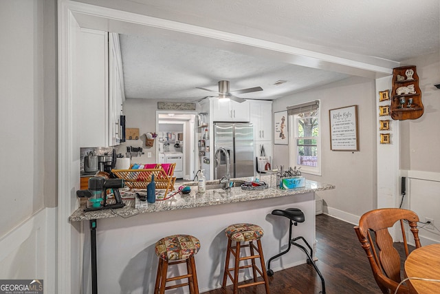 kitchen with appliances with stainless steel finishes, a peninsula, white cabinets, dark wood finished floors, and washer / clothes dryer