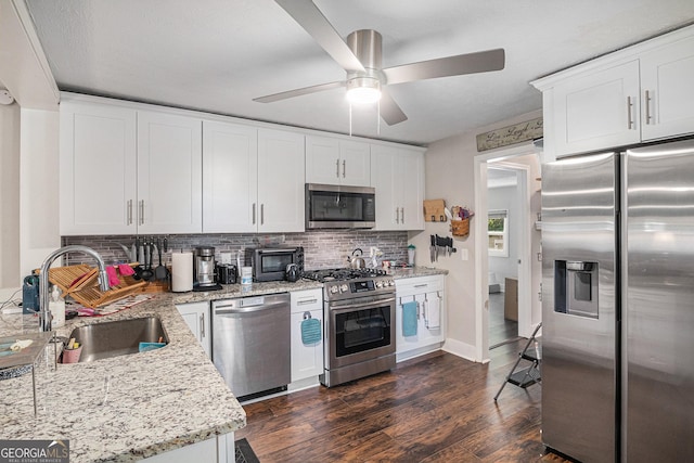 kitchen featuring appliances with stainless steel finishes, a sink, tasteful backsplash, ceiling fan, and dark wood-type flooring