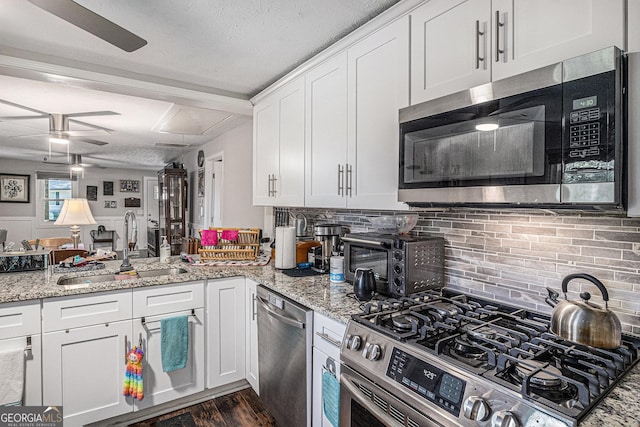 kitchen featuring stainless steel appliances, a ceiling fan, a sink, dark wood-type flooring, and white cabinetry