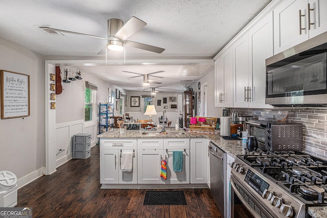 kitchen with appliances with stainless steel finishes, a sink, a peninsula, ceiling fan, and dark wood finished floors