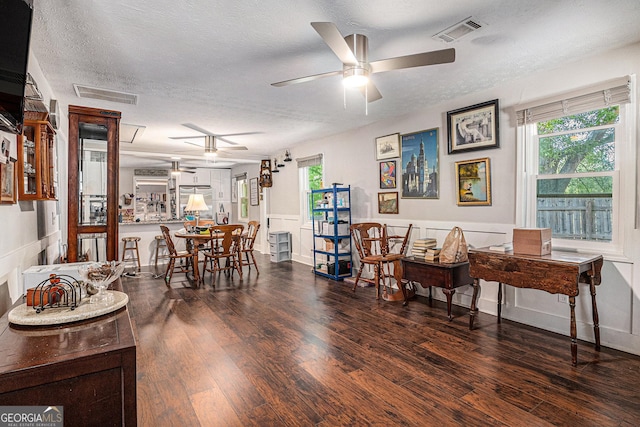 dining area with a ceiling fan, a textured ceiling, wood finished floors, and a wainscoted wall
