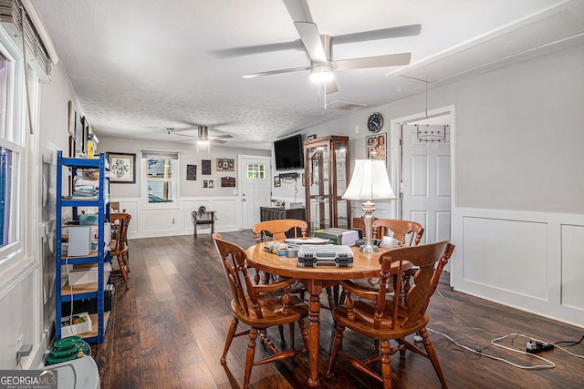 dining area with attic access, a decorative wall, ceiling fan, wainscoting, and dark wood-style floors