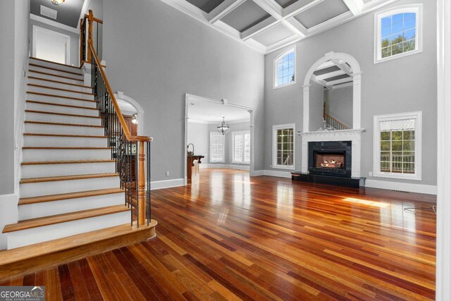 unfurnished living room featuring a lit fireplace, arched walkways, hardwood / wood-style floors, coffered ceiling, and baseboards