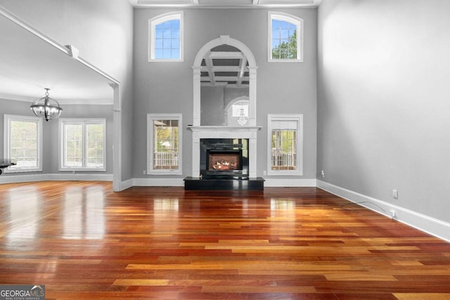 unfurnished living room featuring a chandelier, a high end fireplace, baseboards, and wood finished floors