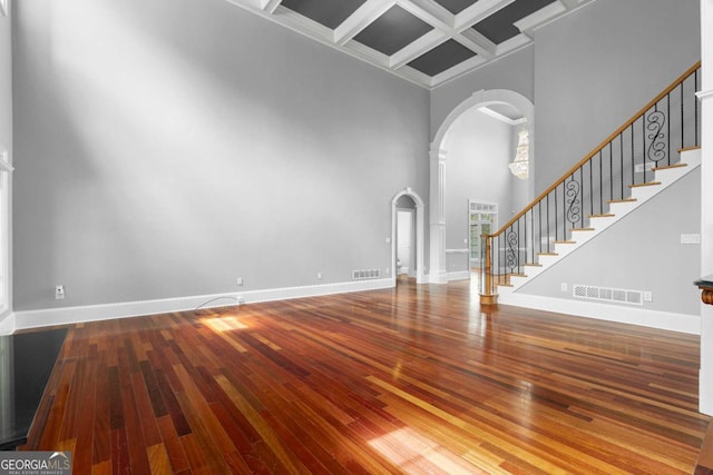 unfurnished living room with arched walkways, visible vents, stairway, coffered ceiling, and baseboards