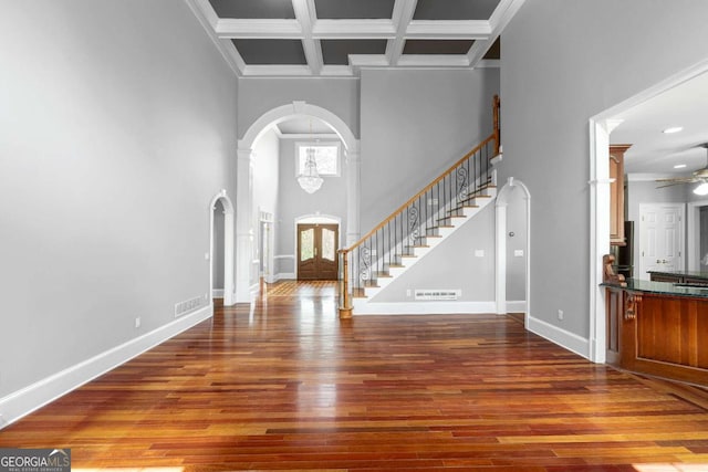 entryway featuring baseboards, arched walkways, coffered ceiling, and wood finished floors