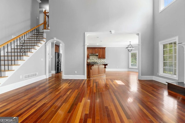 unfurnished living room featuring arched walkways, visible vents, stairway, hardwood / wood-style floors, and baseboards